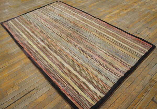 Low-pile rug with thin multicolor stripes and a dark border displayed on distressed wood planks.