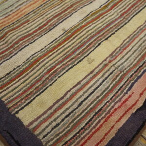 Multicolored striped high-pile rug with bands of cream, red, and dark colors rests on distressed wooden floors.