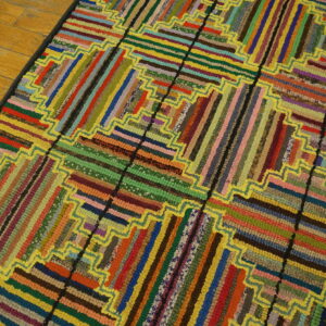 Multicolor braided rug with log cabin strip pattern and bright yellow zigzag outlines rests on light wood flooring.