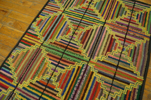 Multicolor braided rug with log cabin strip pattern and bright yellow zigzag outlines rests on light wood flooring.