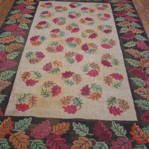 A rug with a cream field and dark leaf border, featuring scattered red, orange, and green fall leaves on wood flooring.