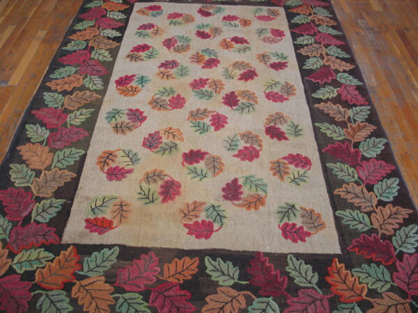 A rug with a cream field and dark leaf border, featuring scattered red, orange, and green fall leaves on wood flooring.