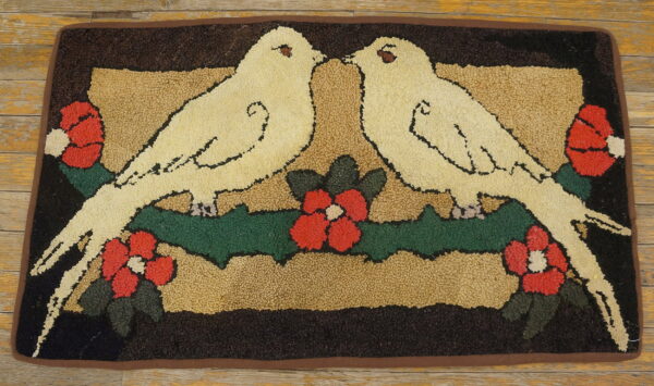 Hooked rug showing two cream doves, red flowers, and green leaves on a dark ground over wood floorboards.