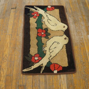 Coarse looped rug featuring a design of two white birds and red flowers on worn wooden planks.