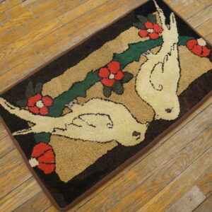 A rectangular hooked rug with doves and red flowers rests on distressed wood plank flooring.