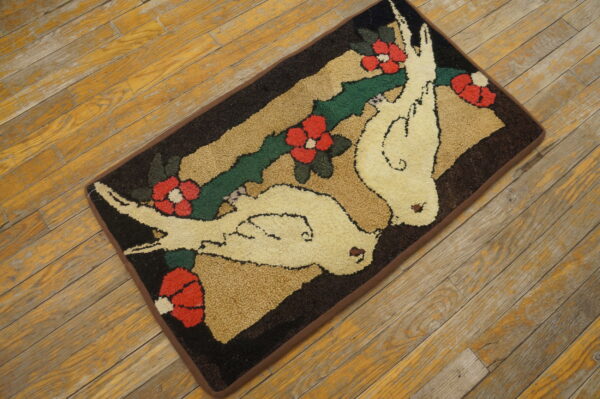 A rectangular hooked rug with doves and red flowers rests on distressed wood plank flooring.