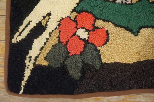 Detail of a hooked rug with a colorful floral pattern in red, cream, green, and navy on a wood floor.