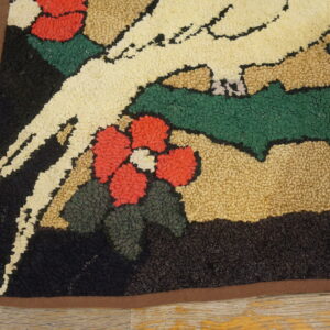 A highly textured rug with a cream bird, red flowers, and green leaves rests on aged wood flooring.
