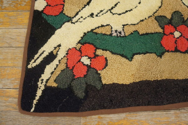A highly textured rug with a cream bird, red flowers, and green leaves rests on aged wood flooring.