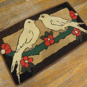 Textured rug with cream birds, red flowers, and green leaves on a dark brown and tan background on wood.