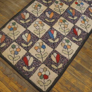 Multi-colored checkerboard rug featuring stylized flowers and buds rests on rustic brown plank wood flooring.