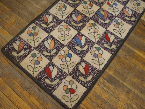 Multi-colored checkerboard rug featuring stylized flowers and buds rests on rustic brown plank wood flooring.
