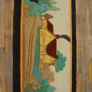 A dimensional rug with a yellow house and trees scene, featuring dark borders, placed on distressed wood.