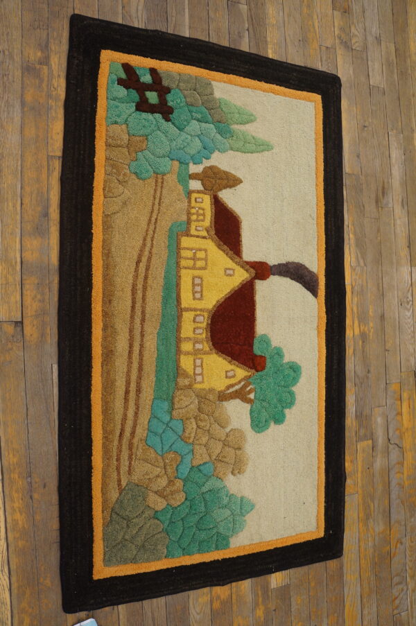 A dimensional rug with a yellow house and trees scene, featuring dark borders, placed on distressed wood.