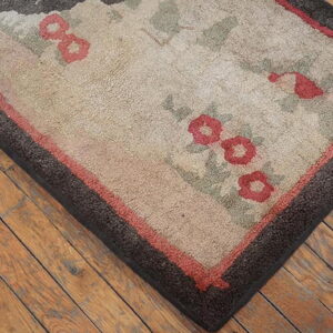 Beige floral rug with red and green accents features a dark brown border resting on wooden floors.