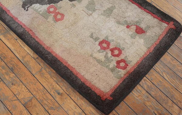 Beige floral rug with red and green accents features a dark brown border resting on wooden floors.