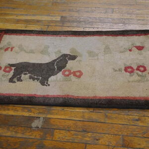 A rectangular mat featuring a dark dog motif and red flowers on a beige ground, bordered in brown, rests on wood planks.