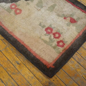 Rustic tan rug with pink and sage floral motifs and dark brown borders rests on distressed wood flooring.