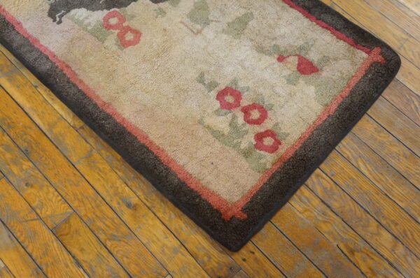 Rustic tan rug with pink and sage floral motifs and dark brown borders rests on distressed wood flooring.