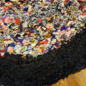 Detail of a highly textured multicolored rag rug edge against a dense black border on light wood planks.