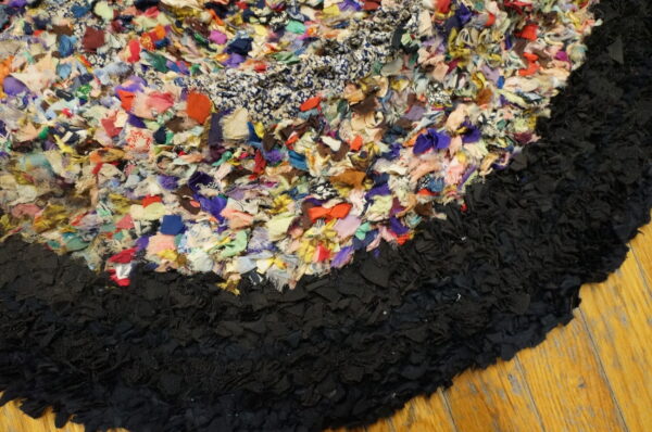 Detail of a highly textured multicolored rag rug edge against a dense black border on light wood planks.