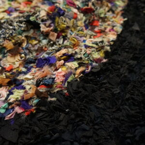 Highly textured rug with multicolored fabric strips adjacent to solid black strips on a wooden floor.