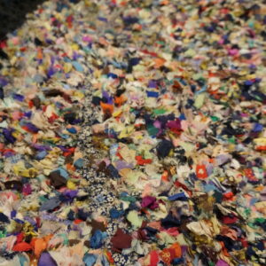 Close-up of a high-pile rag rug made from highly multicolored fabric scraps with a visible black border.