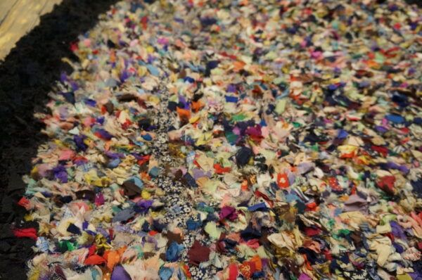 Close-up of a high-pile rag rug made from highly multicolored fabric scraps with a visible black border.