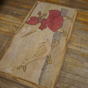 Beige runner rug with a red and peach figure and bird design resting on distressed wood planks.