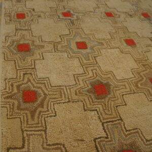 Textured beige rug featuring geometric patterns outlined in brown, red, and subtle blue, next to wood planks.