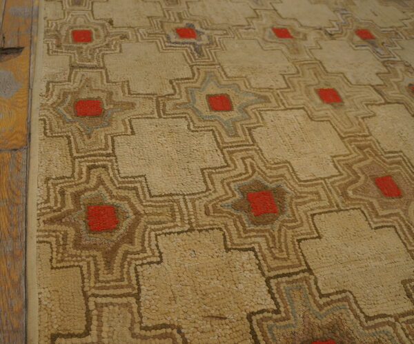 Textured beige rug featuring geometric patterns outlined in brown, red, and subtle blue, next to wood planks.