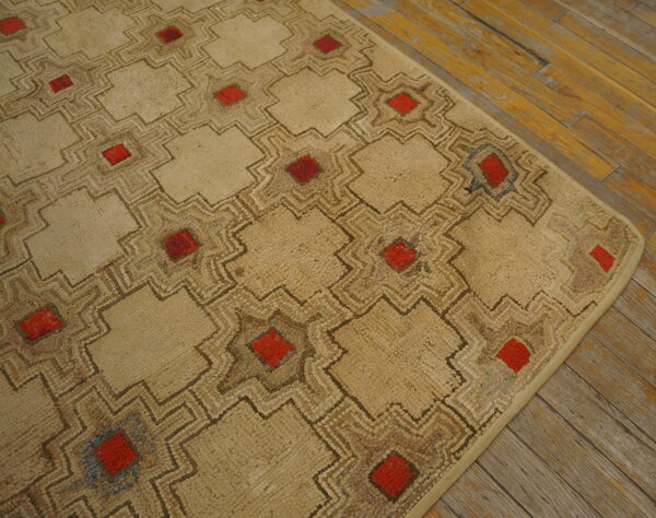 Textured beige rug with an interlocking geometric pattern, red squares, and exposed plank wood flooring.