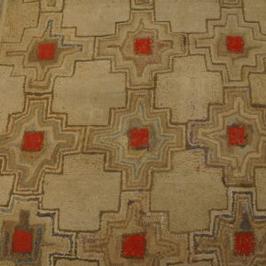 Beige low-pile rug with geometric patterns featuring red centers and brown outlines rests beside wooden planks.