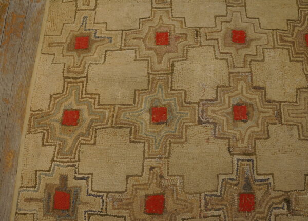 Beige low-pile rug with geometric patterns featuring red centers and brown outlines rests beside wooden planks.