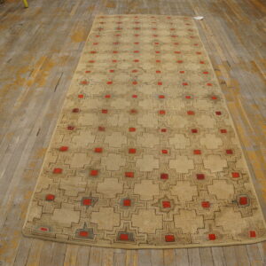 Beige runner rug with brown outline geometric pattern and bright red squares on distressed wood floor.