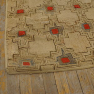 Beige rug with a repeating brown, blue, and red geometric motif resting on worn wood plank flooring.