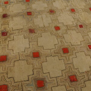 Textured beige rug with a stepped geometric grid pattern featuring central red squares on a distressed wood floor.