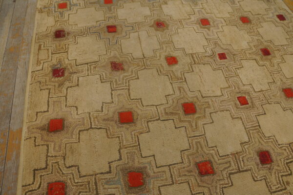 Textured beige rug with a stepped geometric grid pattern featuring central red squares on a distressed wood floor.
