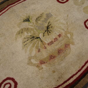Cream rug with visible hooked texture, a muted floral center, and bold red coiled borders on wood flooring.