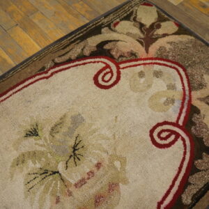 Textured beige rug with complex floral motifs and a deep red scrolled border rests on hardwood floor.