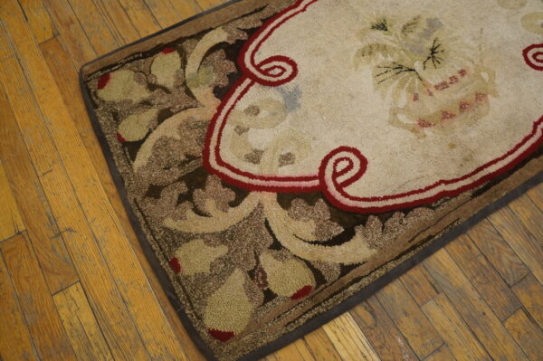 Cream, brown, and red rug with a prominent floral pattern and looped texture on distressed wood plank flooring.