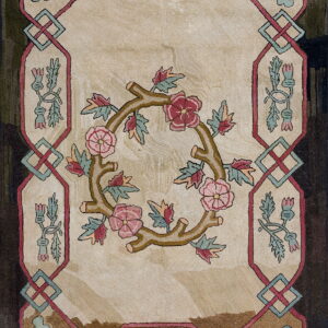 Cream and brown rug featuring a central rose wreath and an intricate border with teal and pink knots.