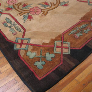 Floral rug corner featuring pink roses, teal vines, and geometric shapes against a tan field on hardwood.
