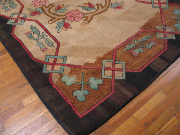 Floral rug corner featuring pink roses, teal vines, and geometric shapes against a tan field on hardwood.