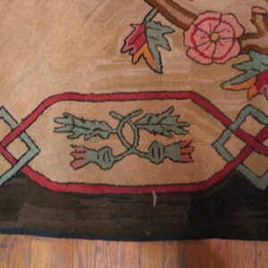 Detailed view of a tan rug with pink floral, green, and red geometric patterns resting on wood floor.
