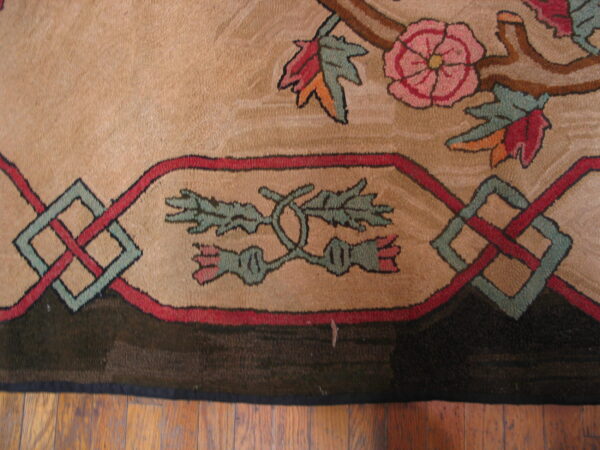Detailed view of a tan rug with pink floral, green, and red geometric patterns resting on wood floor.