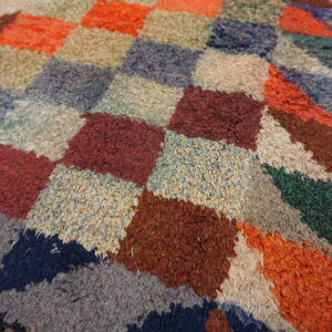 High-pile rug surface showing a geometric patchwork of blue, red, orange, and cream textured blocks.
