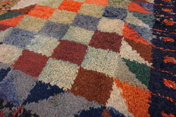 High-pile rug surface showing a geometric patchwork of blue, red, orange, and cream textured blocks.