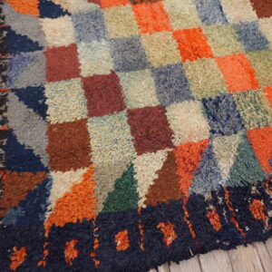 A colorful, high-pile rug with a checkerboard and geometric pattern rests on rustic wood flooring.