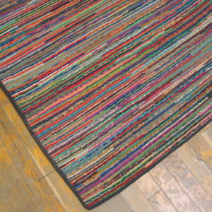 Multicolor low-profile rug with thin linear stripes resting on worn light wood flooring.